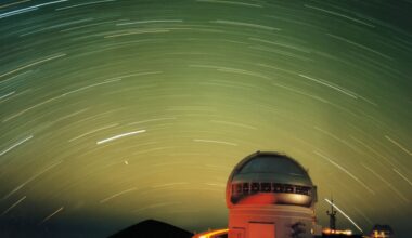 A series of white streaks move in a circular fashion in a green night sky all over the lit up dome of an observatory at the bottom right of the image.