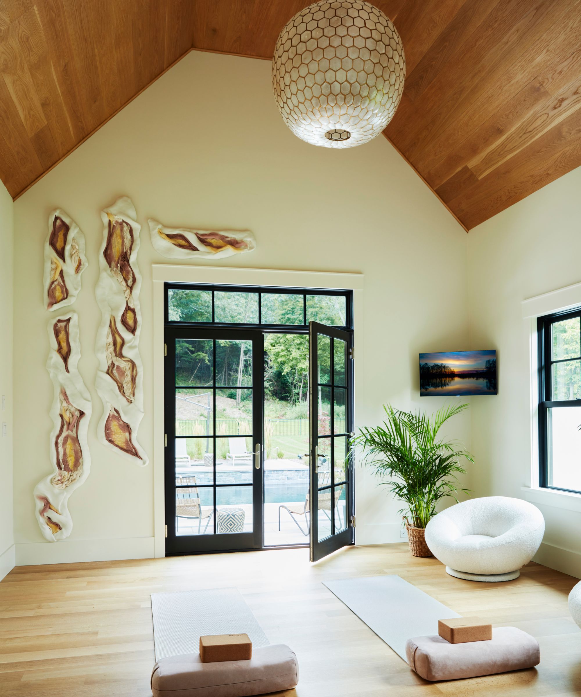 at home yoga studio room in a project designed by camden grace with neutral walls, light wood floor, warmer wood vaulted ceiling and black crittal patio doors onto the pool