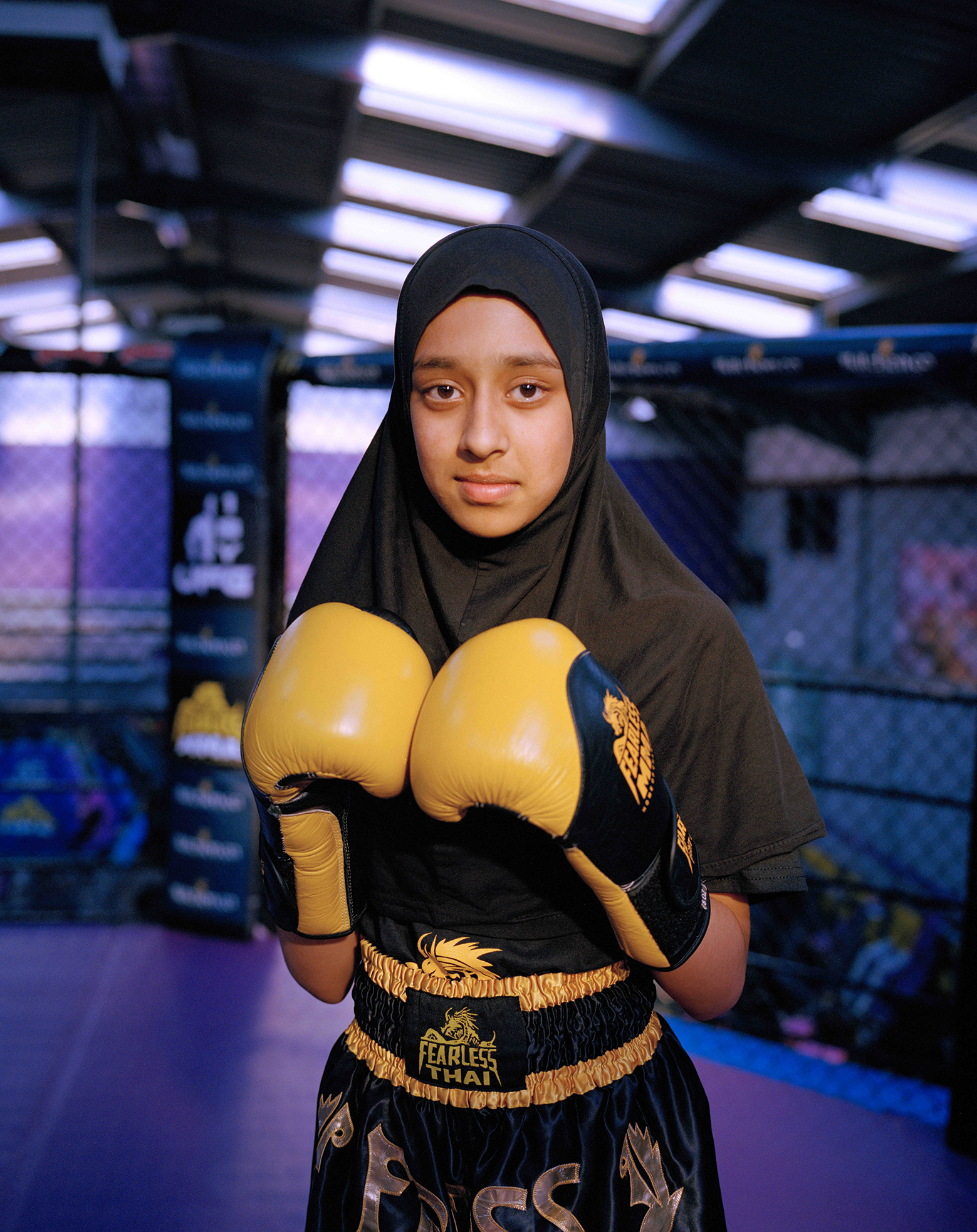 A person dressed in black sports attire wears yellow boxing gloves, ready for training in a vibrant gym setting