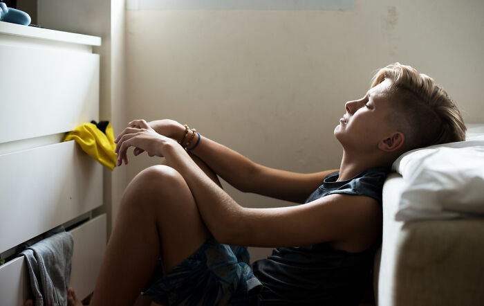 Teenager sitting on the floor in a dim room, looking distressed, illustrating confusion between Dr. Google and a real doctor.