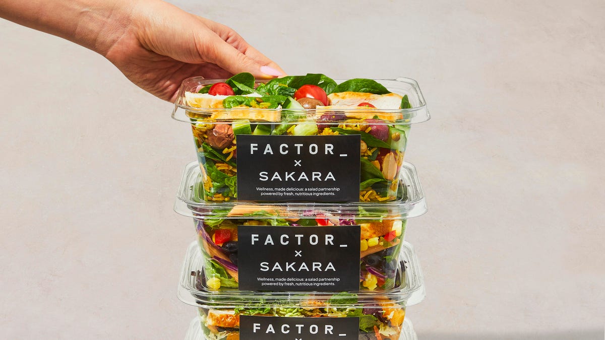 three salads in plastic containers with black labels stacked on top of each other