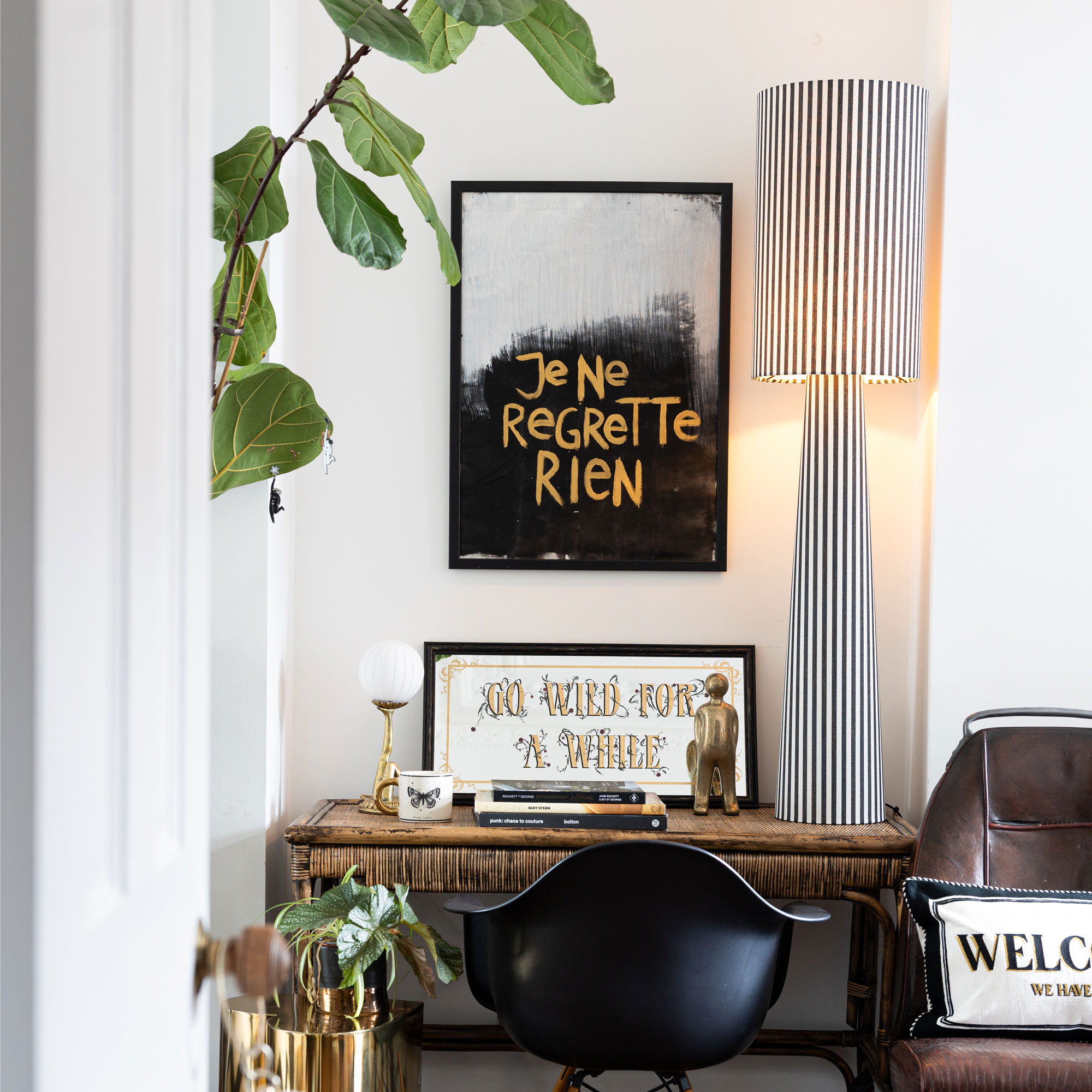 White walls room with bamboo desk and black and white striped floor lamp and black frame picture on the wall.