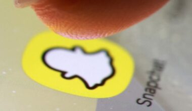 A finger hovers over the Snapchat app icon on a smartphone screen in a close-up view.