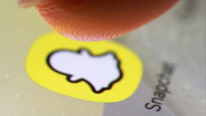 A finger hovers over the Snapchat app icon on a smartphone screen in a close-up view.
