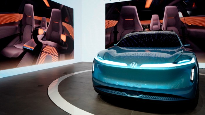 Volkswagen AG ID.CODE concept electric vehicle on display, with a digital rendering of its interior shown on a large screen behind it