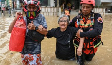 Two rescuers help an older woman wade through waist-deep floodwater in Hat Yai district, in southern Thailand