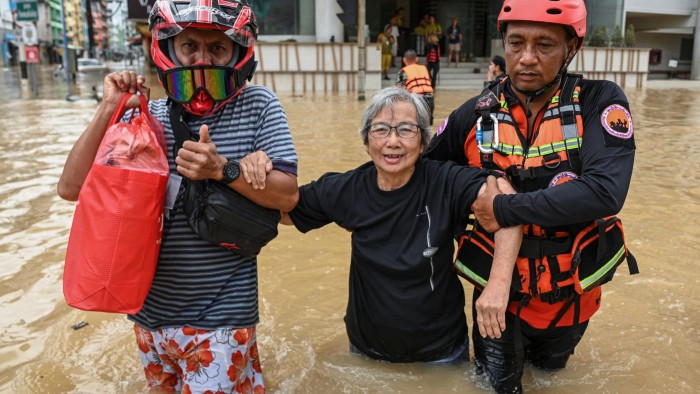 Two rescuers help an older woman wade through waist-deep floodwater in Hat Yai district, in southern Thailand