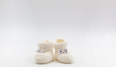 Knitted white baby booties with polka-dot bows on a gray isolated background.