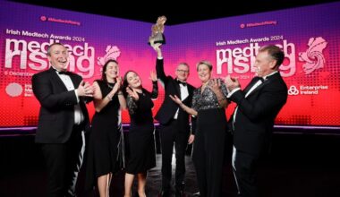 A group of people dressed up in black tie cheering on stage holding an award. A screen behind them says Medtech Rising.