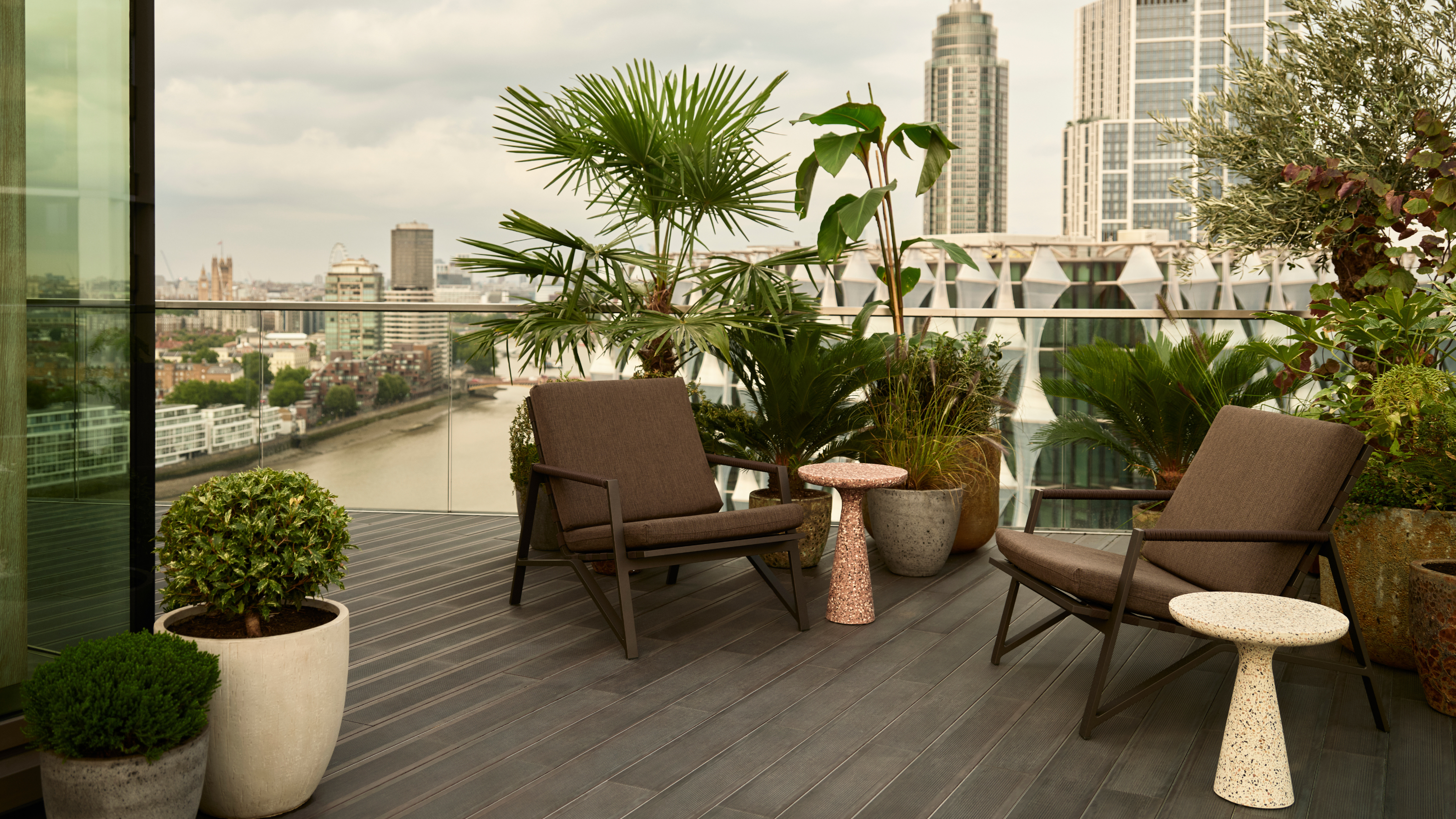 A contemporary private terrace overlooking the London skyline with seating, side tables and an arrangement of tropical plants