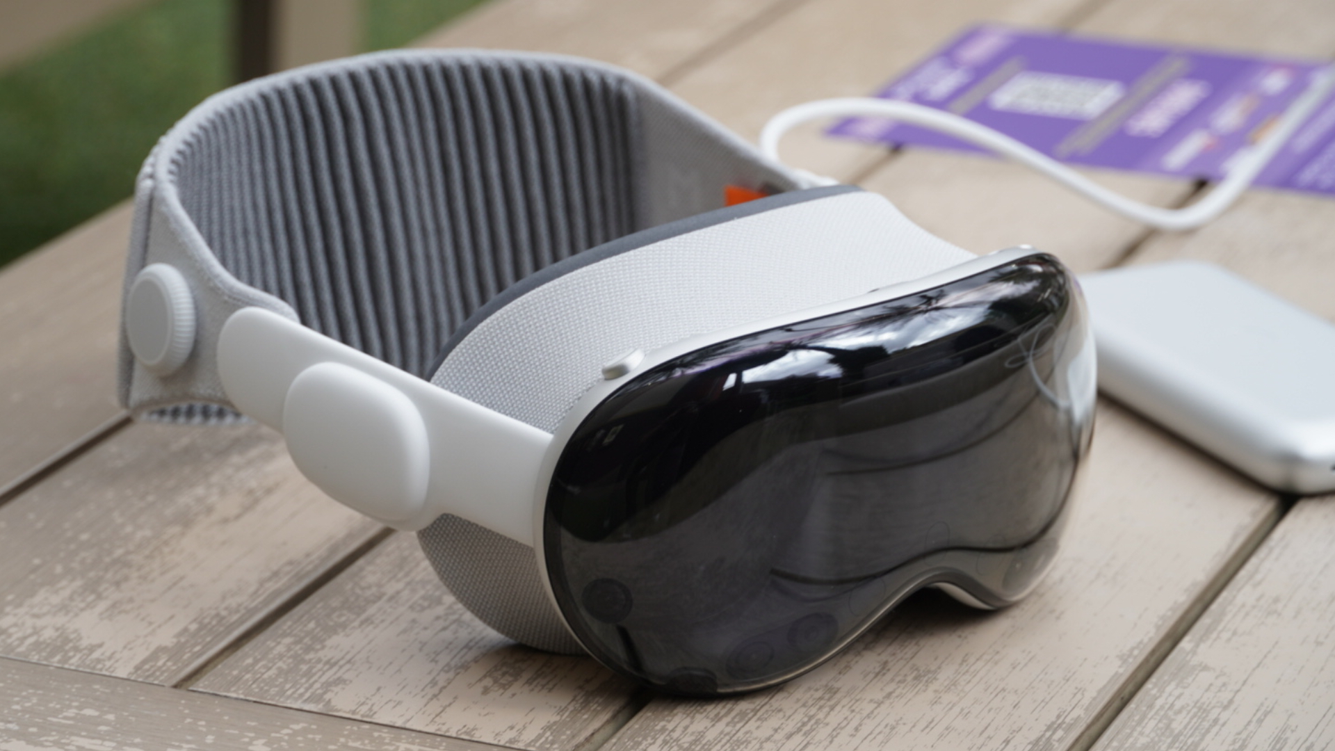 Apple Vision Pro outdoors on a table with accessories.