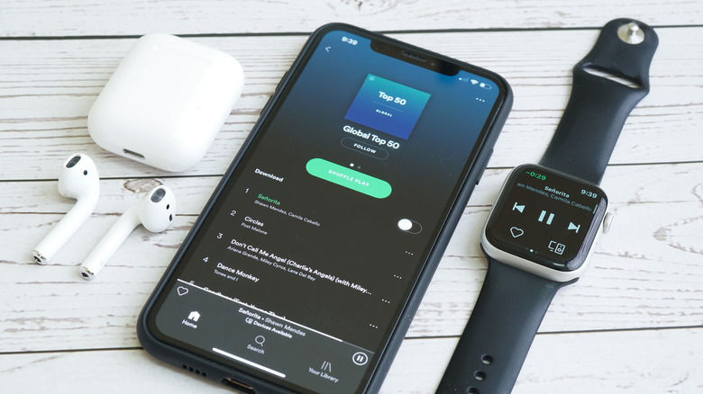 AirPods, iPhone, and Apple Watch lined in a row with the Spotify app.