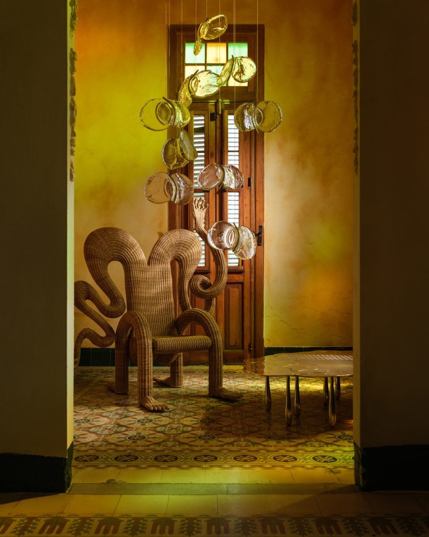 A fantastical wicker chair, a metal table and a glass chandelier in an ochre-hued room
