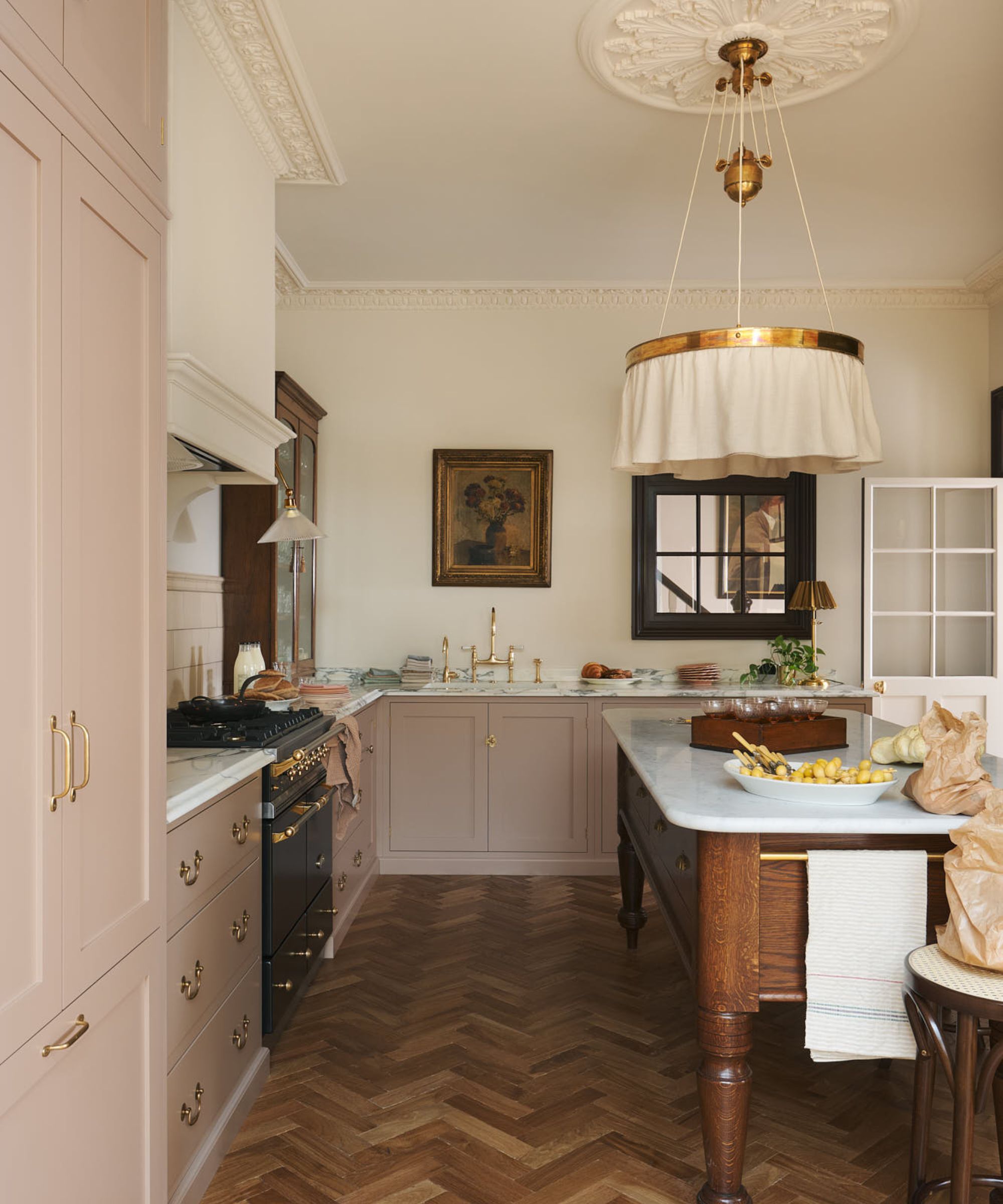 A neutral kitchen with white walls, muted pink cabinets, a wooden prep table, and vintage decor