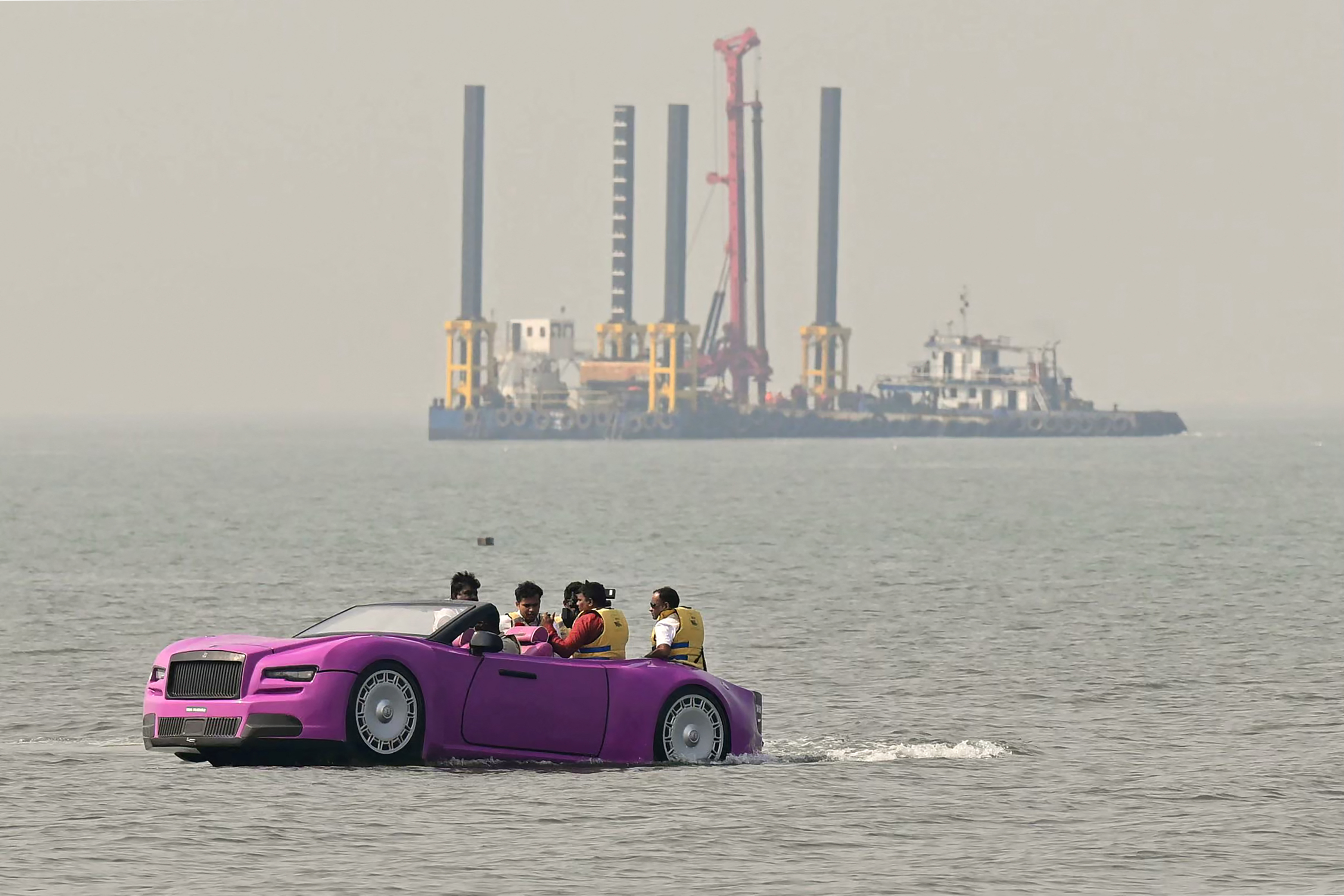 Tourists in life vests ride a purple jet car boat across the Arabian Sea with a cargo ship in the background.