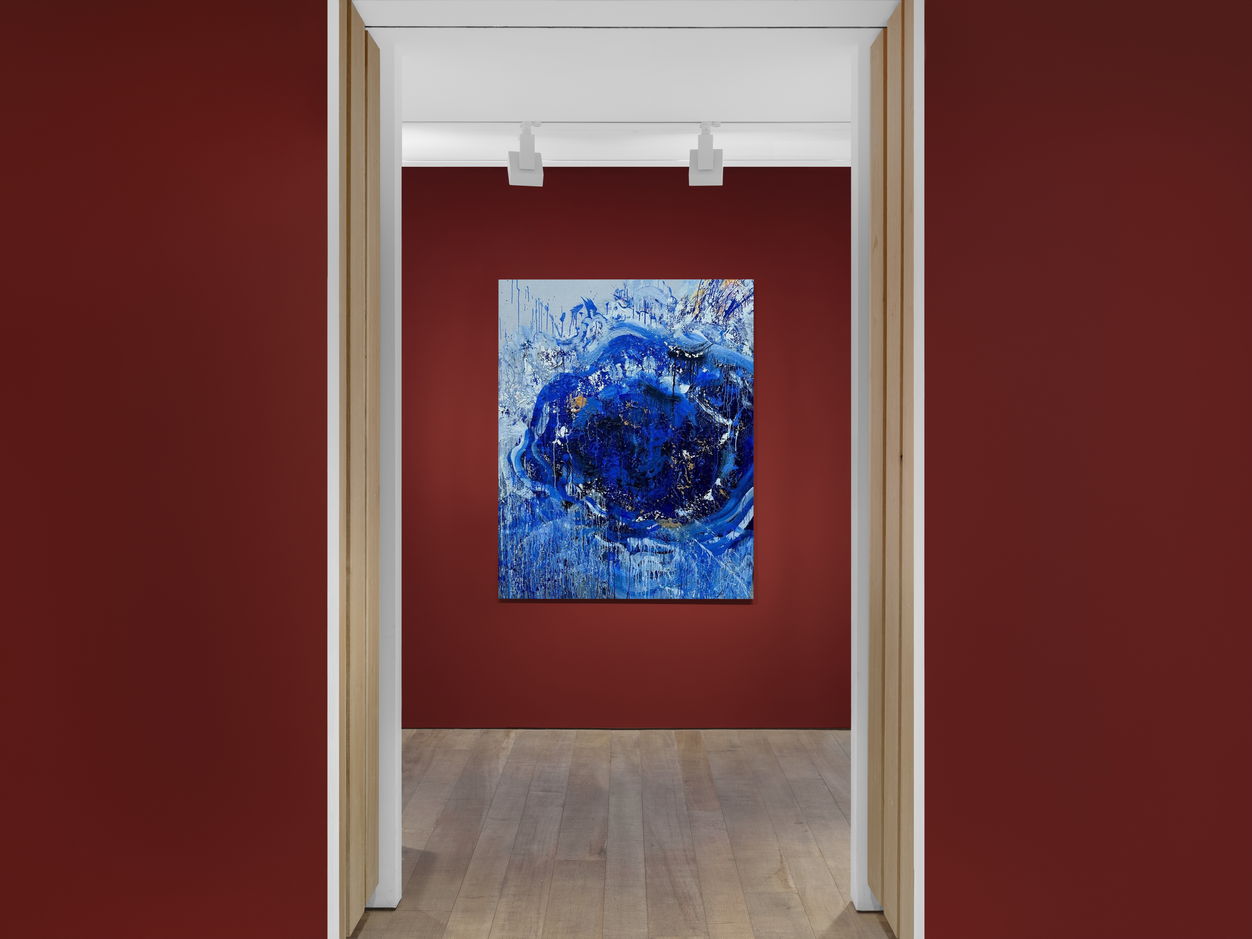 View through a doorway into a room with a blue abstract painting on a red wall.