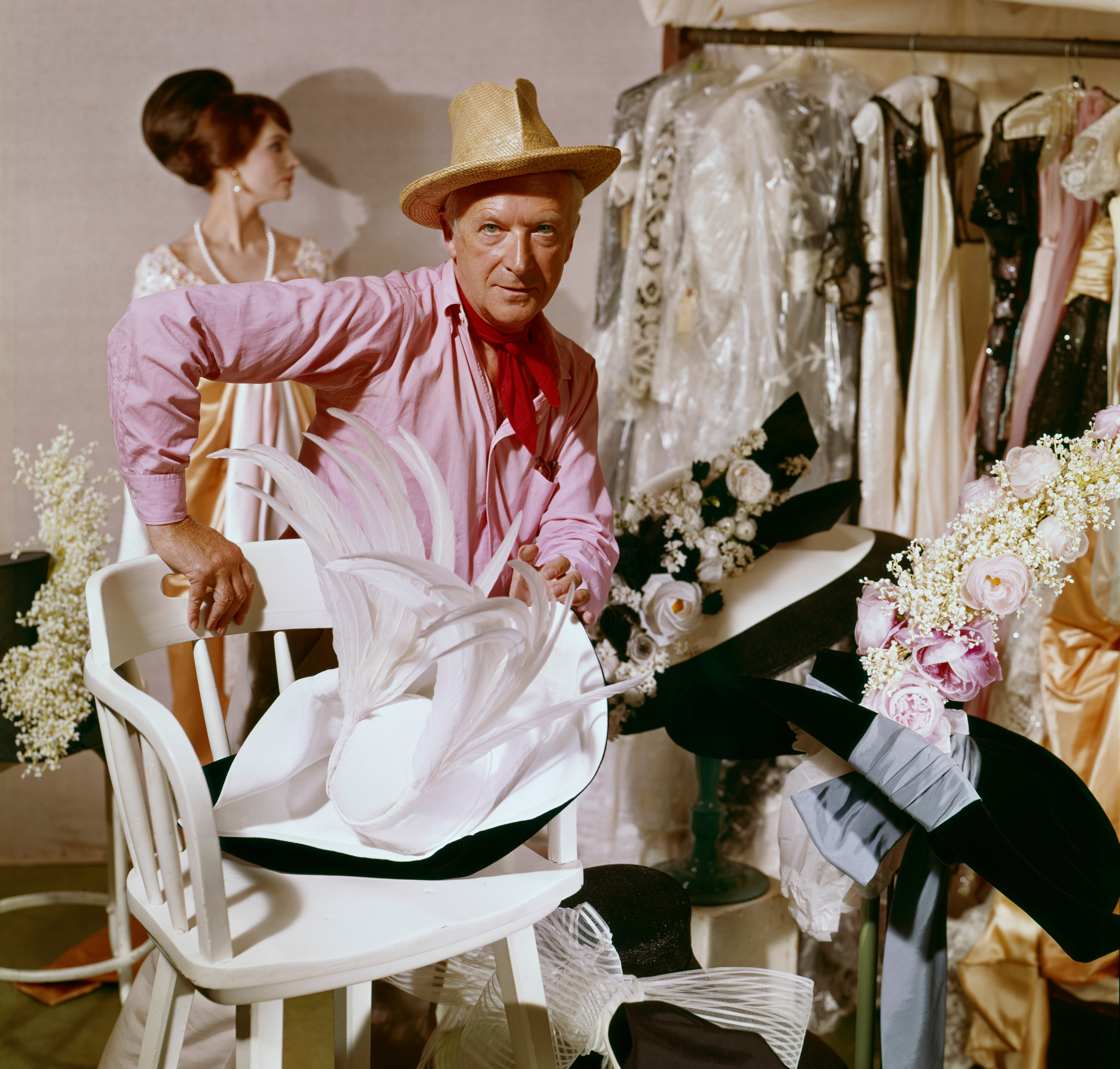 Cecil Beaton working on My Fair Lady in 1963, surrounded by costume elements and a woman in a costume in the background.