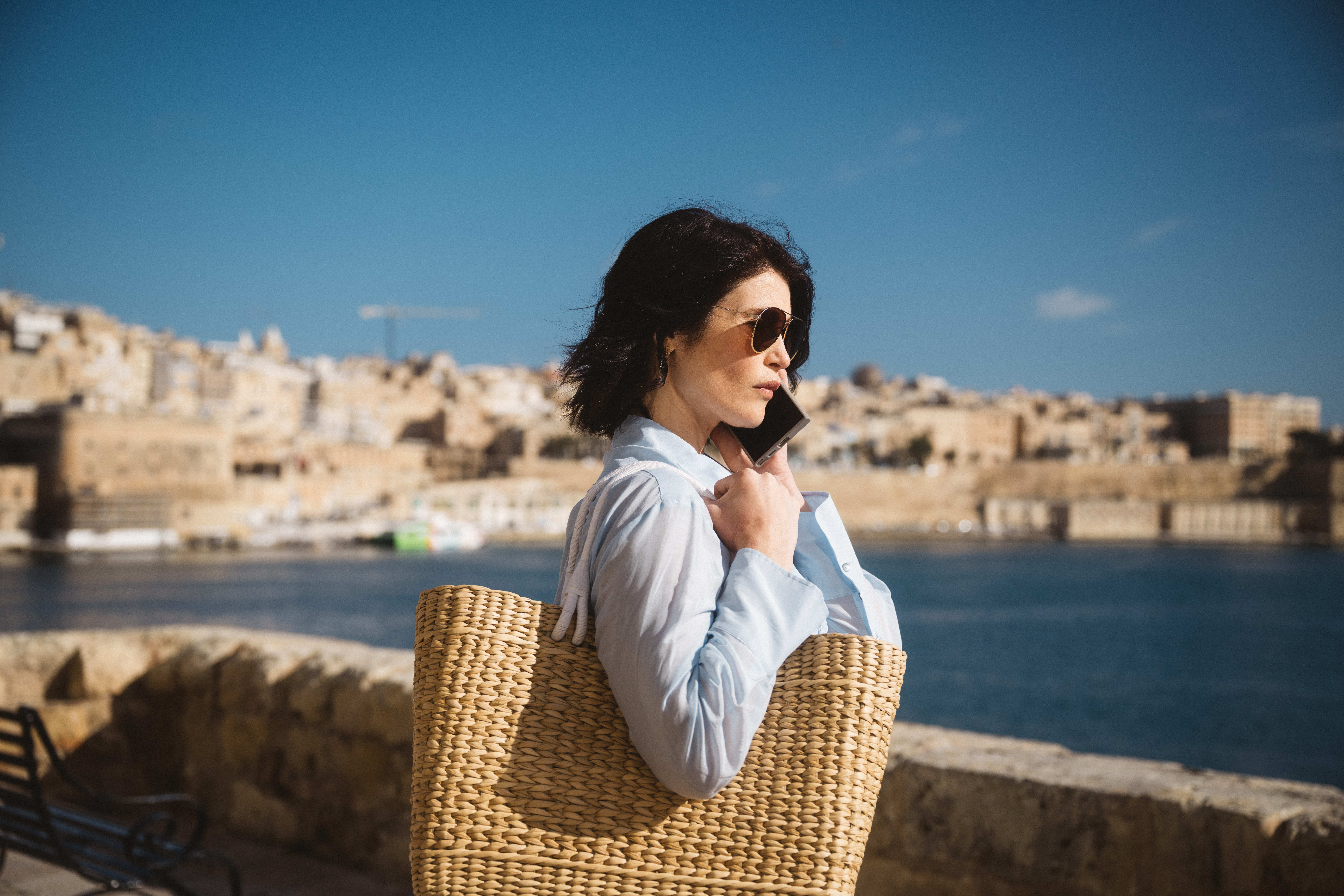Gemma Arterton as Kate Henderson in Secret Service, talking on a phone while sitting in a wicker chair outdoors with a harbor in the background.