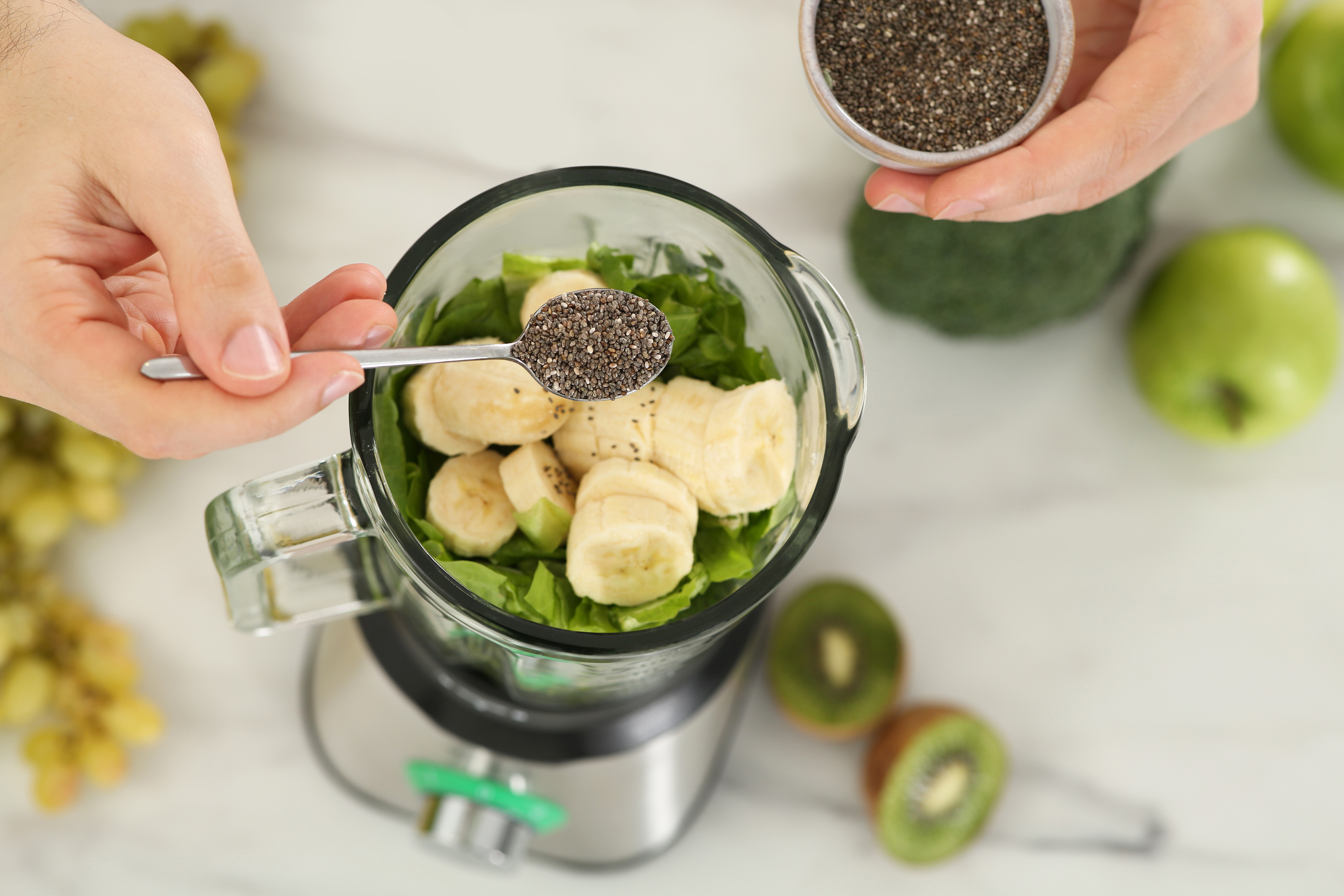 Man adding chia seeds to a blender with ingredients for a smoothie.