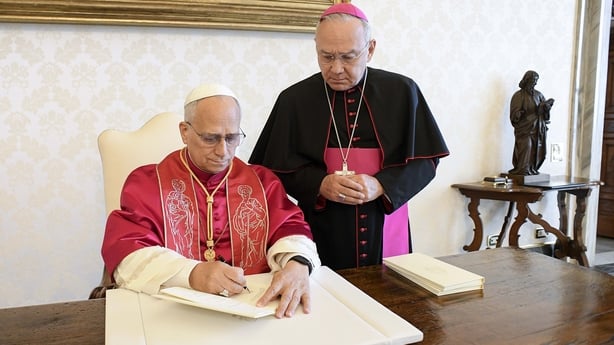 Pope Leo XIV signs his Apostolic Exhortation 'Dilexi te' at a desk in the presence of Archbishop Edgar Peña Parra.