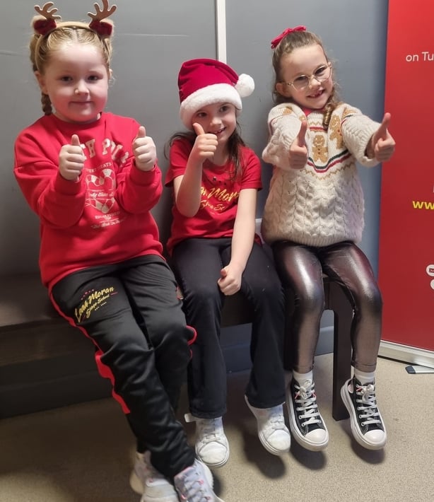 Three children sit together in Christmas jumpers
