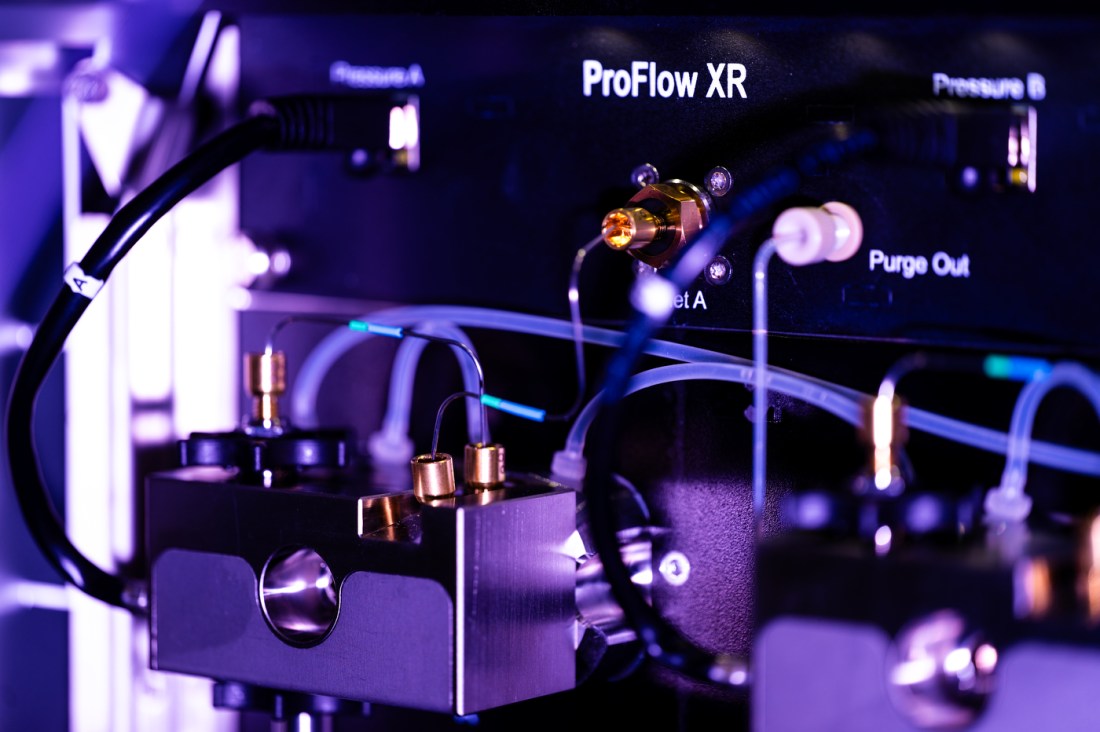 Close-up of laboratory instrumentation with illuminated tubes, wires, and connectors attached to a device labeled “ProFlow XR,” glowing under purple and blue lighting.