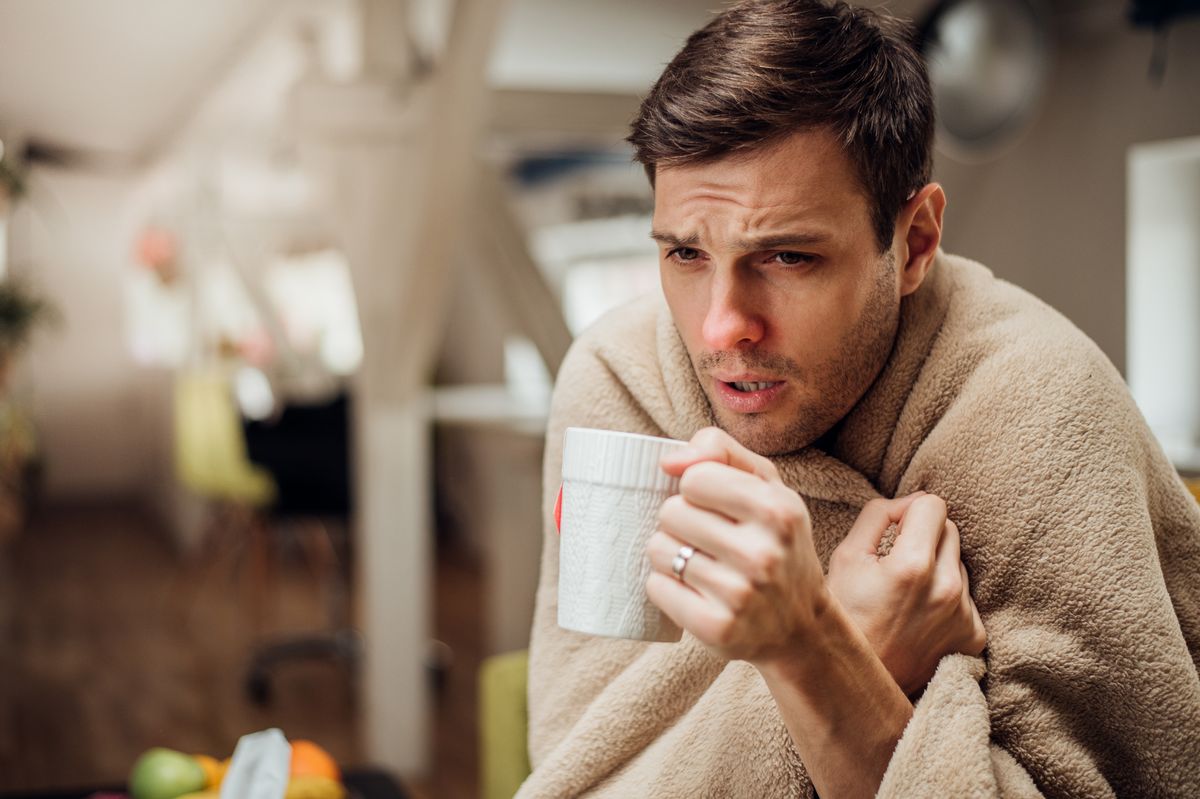 Young man shivering under the blanket and drinking tea