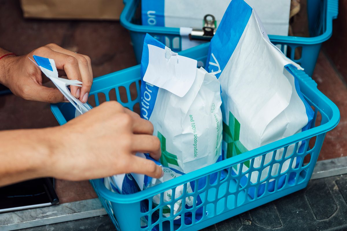An unrecognizable person putting paper bags filled with prescription medicine, into a basket in a van