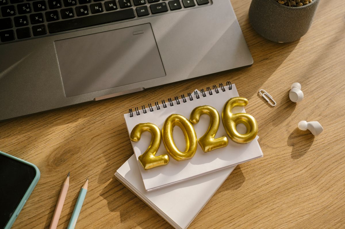 Note pad with golden digits 2026 on wooden work desk. Planning resolutions for New Year 2026. Laptop, note pad, phones, pencils
