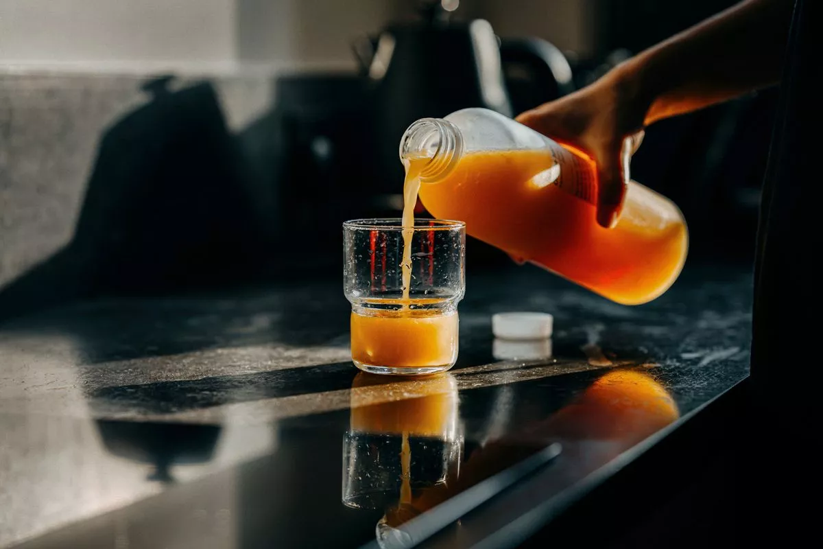 Cropped shot of a female hand pours a plastic bottle of fresh orange juice