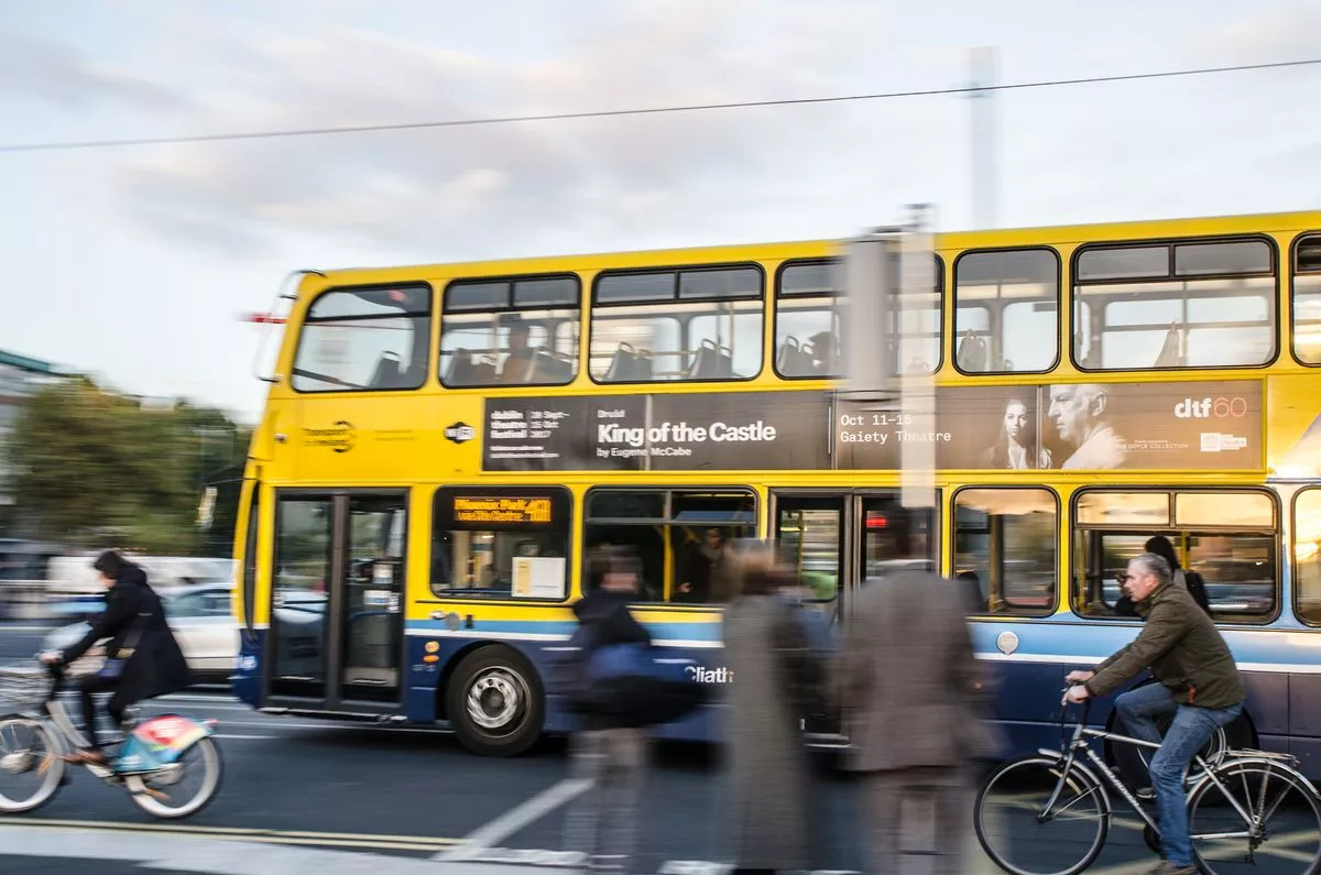 Side view of cyclists besides of a double-decker bus in downtown O'Connell street of Dublin Ireland during rush hour a day of autumn. There are blurred pedestrians on foreground
