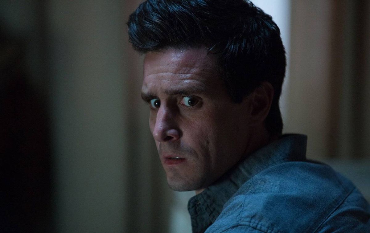 An individual with a serious expression, dressed in a blue shirt, is gazing intently into the distance within an indoor setting.