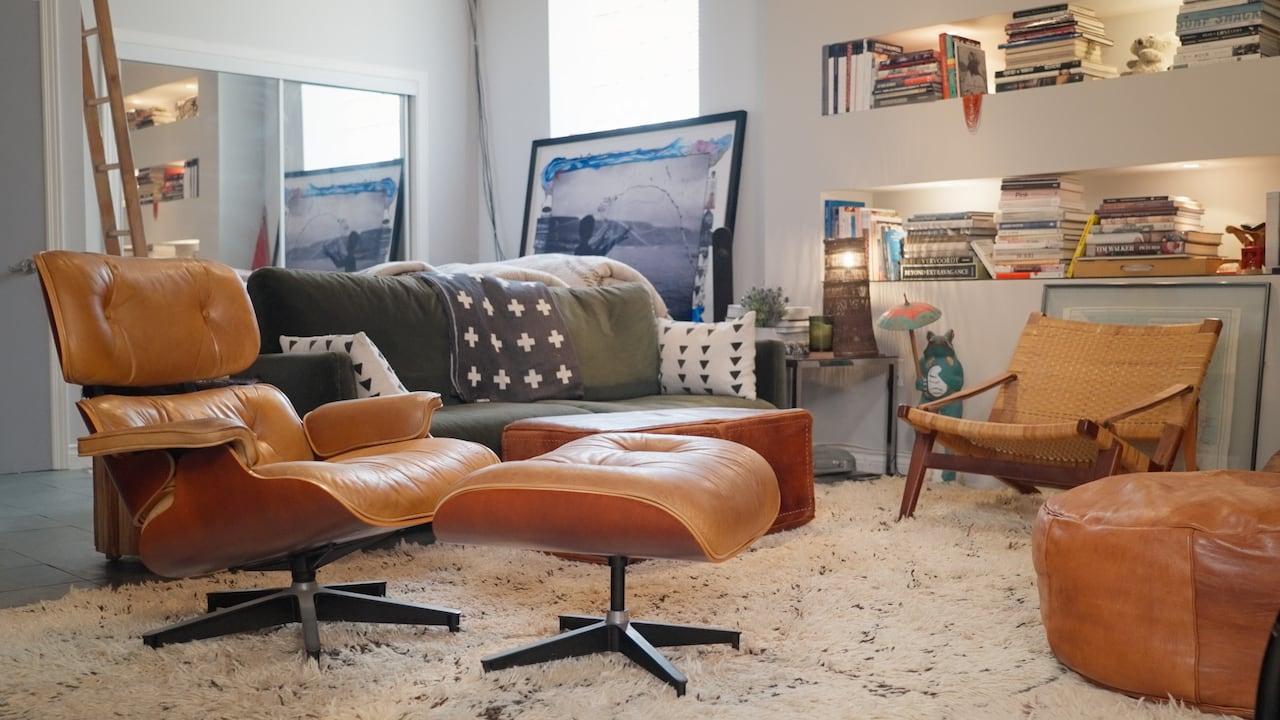 A living room with a closeup on a leather lounge chair with a couch and bookshelves in the background. 