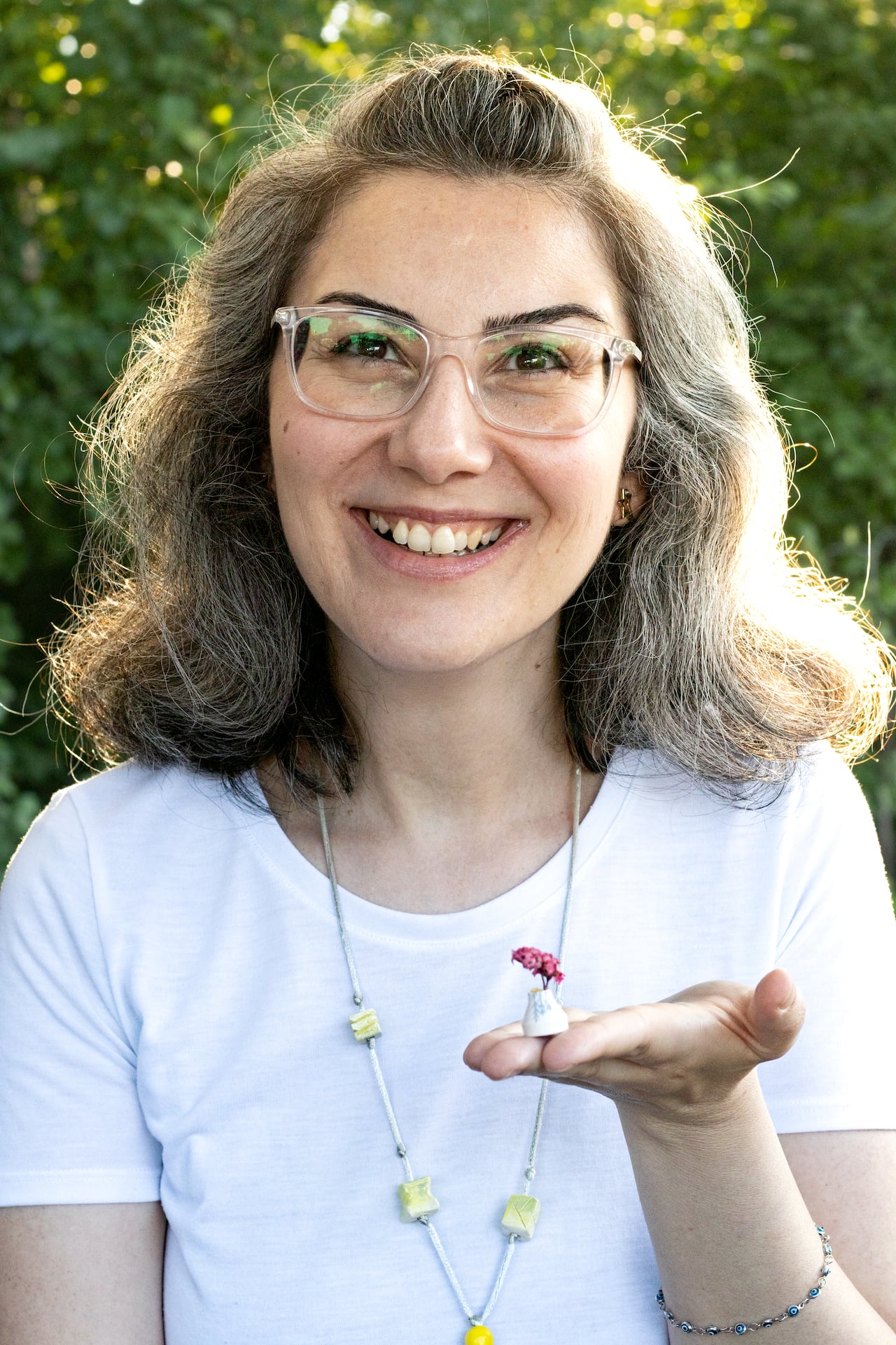 Selen Kaplan, in a white shirt with glasses and shoulder length salt and pepper hair, holding one of her miniature vases