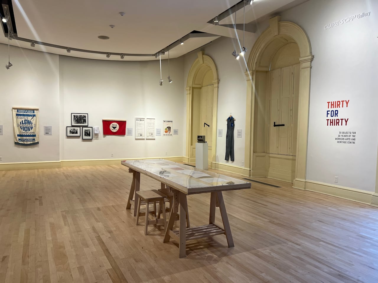 In a large white room with high ceilings and large windows, banners, photos and a uniform are displayed on the walls. A display table sits at the centre of the room.