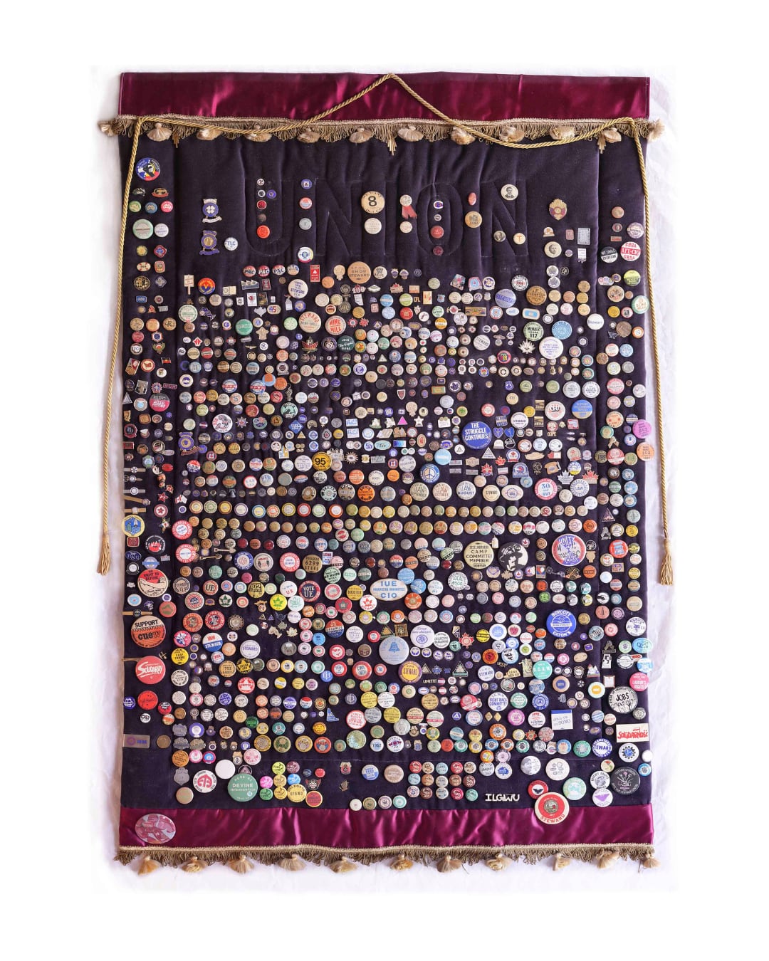 The full-length photo shows a black piece of fabric trimmed with red material and gold tassel. It is decorated with hundred of buttons and pins. The word "Union" is stitched into the background. 