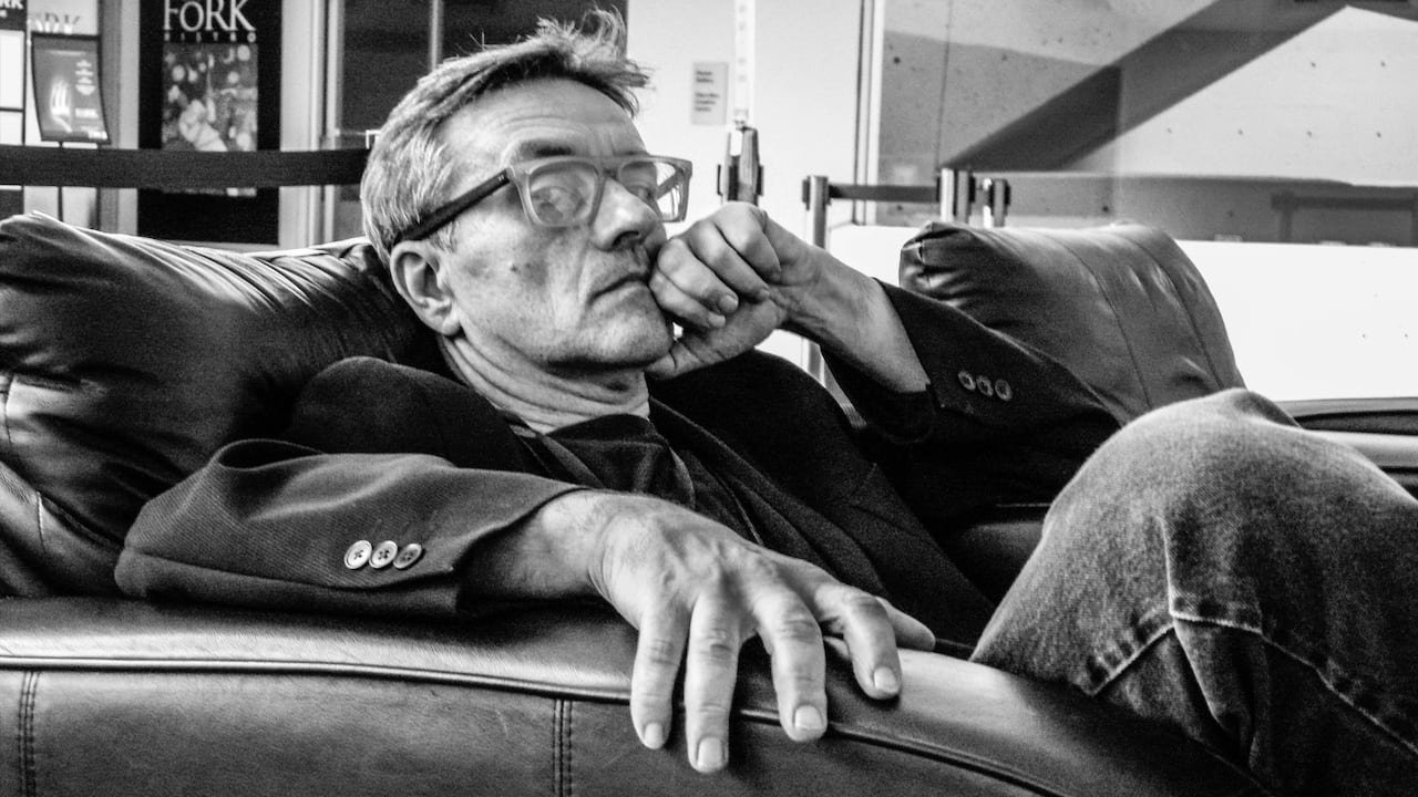 A man in glasses, posing on a couch for a headshot.