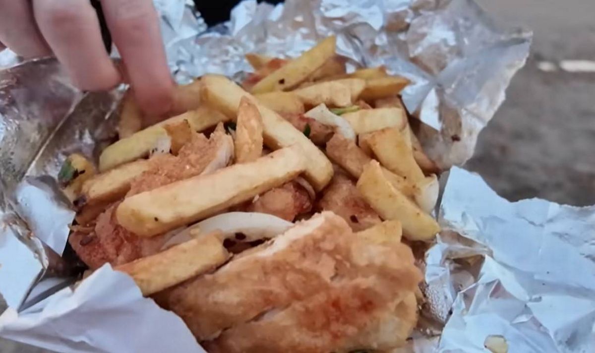 An individual holding a foil-wrapped package containing fish and chips, consisting of golden-brown French fries and a piece of breaded fish, possibly being served as a meal.