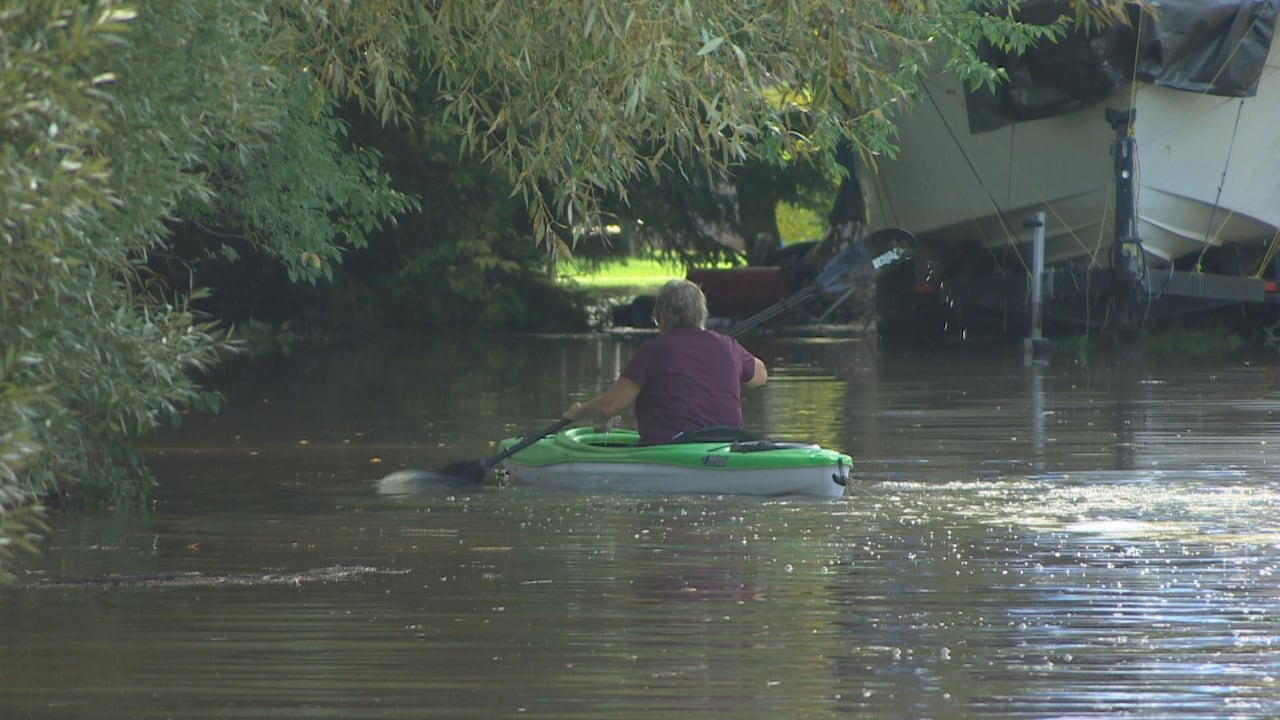 A woman is seen from the rear, paddling away in a kayak down a flooded street.