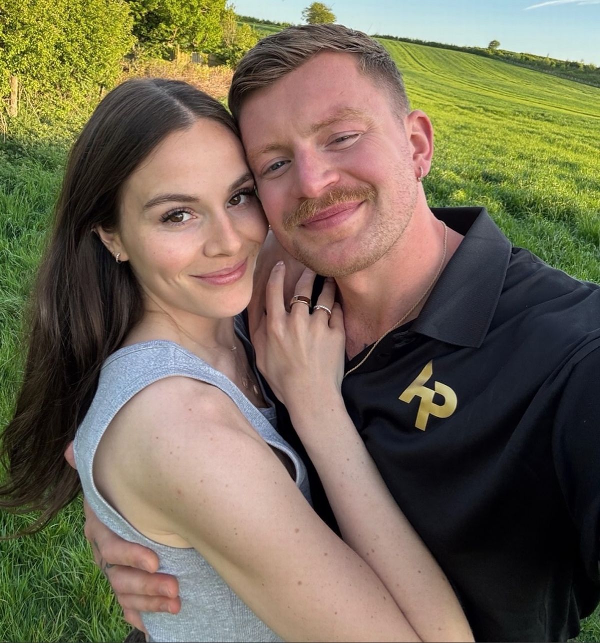 Adam Peaty and Holly Ramsay smiling in a field