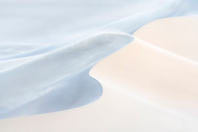 Soft, abstract landscape of pale sand dunes with smooth, flowing curves in shades of white and light blue, creating a tranquil and minimalist scene.
