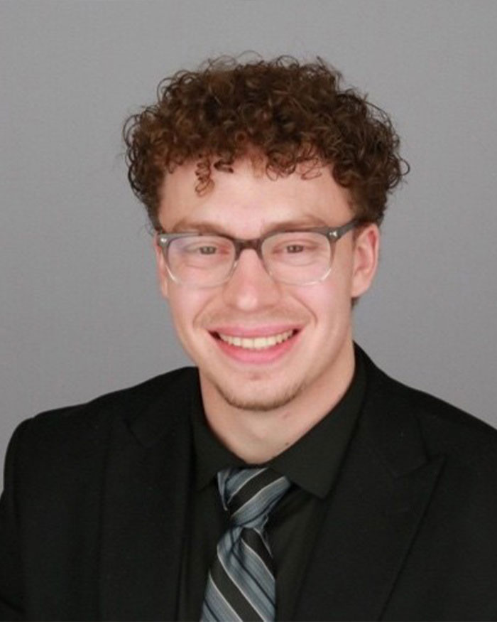 Young man with curly hair and glasses wearing a suit and tie, illustrating ChatGPT expert concerns after tragic incident.