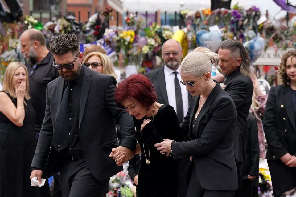 Jack, Sharon and Kelly Osbourne embrace as they view the messages and floral tributes left at the Black Sabbath Bridge bench in Birmingham (Joe Giddens/PA)