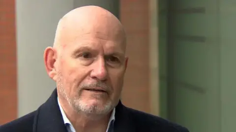 A man is outside. He has a navy coat on and a shirt.