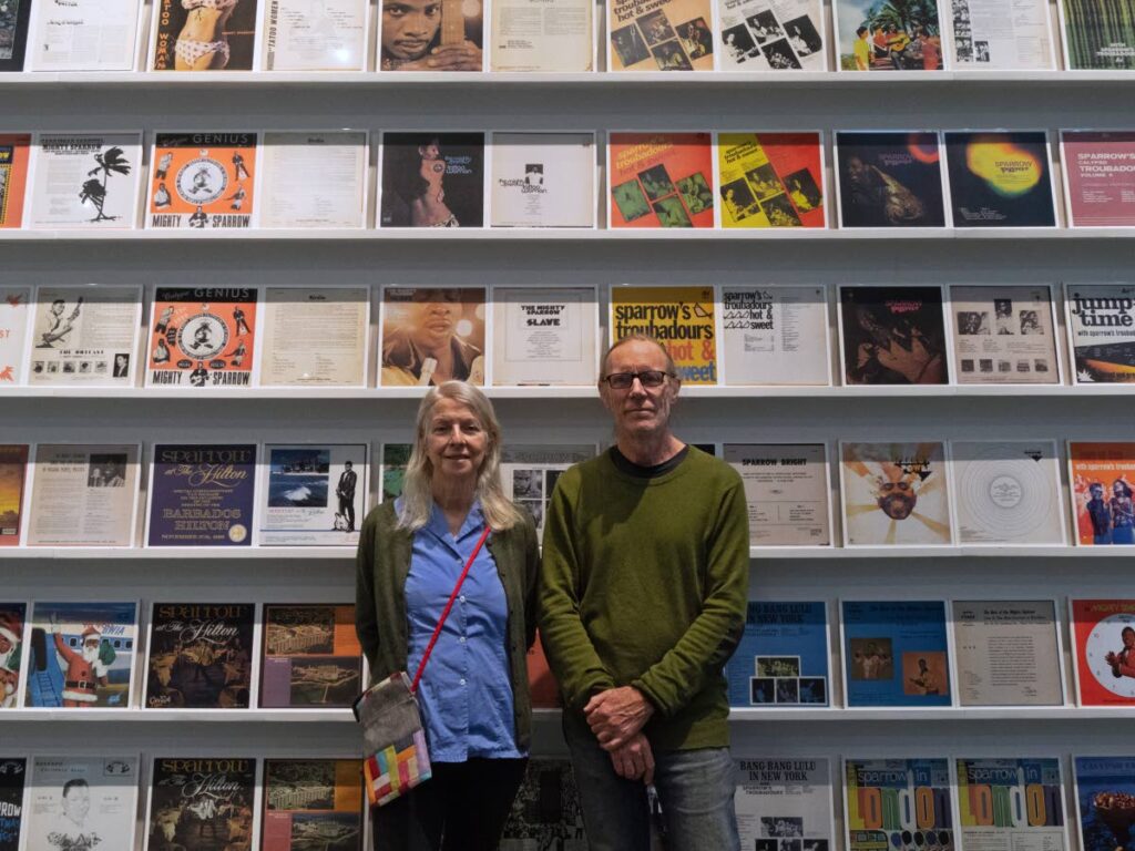 Visual artists Carmel Buckley and Mark Harris in front of 360 full-size ceramic tiles of the front and back covers of 180 Mighty Sparrow albums and 12-inch singles on display at the Weston Art Gallery in Cincinnati, Ohio. - 