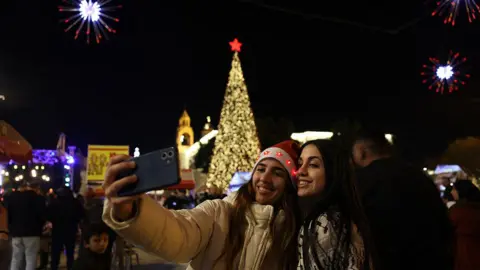 Getty Images Two women take a photo in front of the Christmas tree in Nativity Square in Bethlehem in the occupied West Bank.