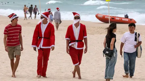 Getty Images People wearing Santa costumes walk along the sand of Bondi Beach in Sydney, Australia on 25 December 2025.