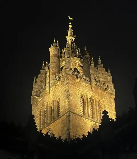 Emma Swift St Giles Cathedral in Edinburgh at night. The cathedral is bathed in golden light and appears to be suspended in mid-air due to way the photo was taken