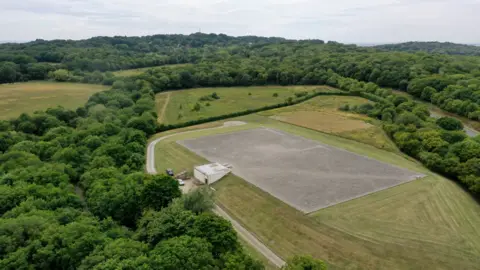 Northumbrian Water Group A drone shot of an Essex and Suffolk Water partially underground reservoir. It is surrounded by green trees.