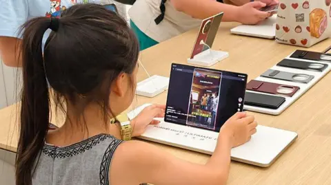 Getty Images A young girl with a pony tail is watching social media videos on a three fold mobile phone at Huawei's world's largest flagship store in Shanghai, China